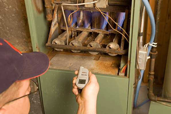 a repairman with digital infrared thermometer checks gas furnace output temperature
